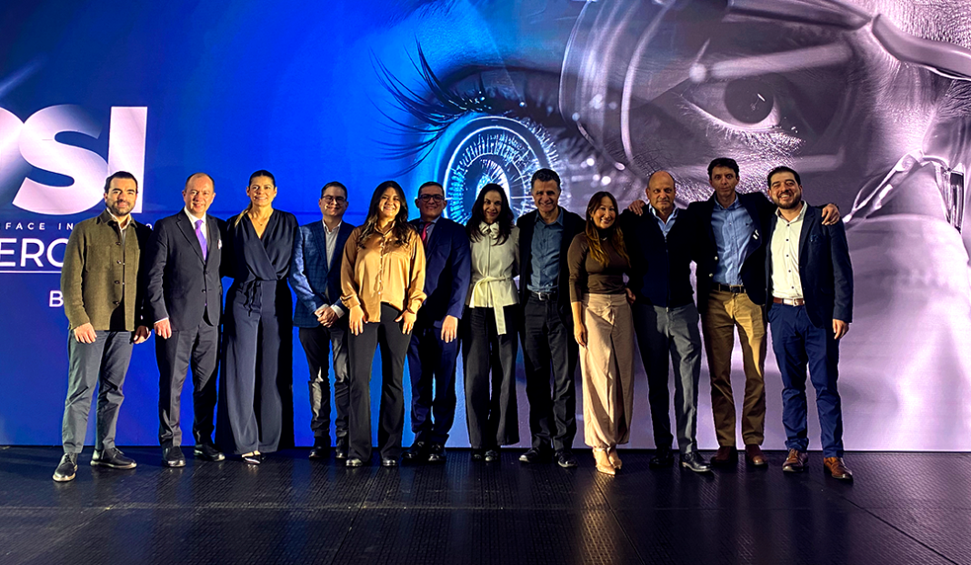 Group of twelve well-dressed professionals standing side by side on a stage, posing for a photo in front of a blue backdrop with a large eye graphic.