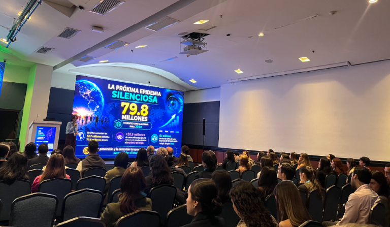 Audience seated in a conference hall as a speaker presents a large blue slide about the next silent epidemic, noting 79.8 million in bold yellow text.