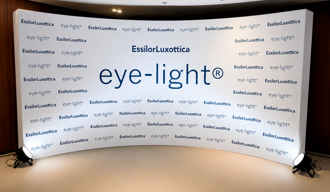 Curved white backdrop with large 'eye-light' logo center and EssilorLuxottica branding around it.