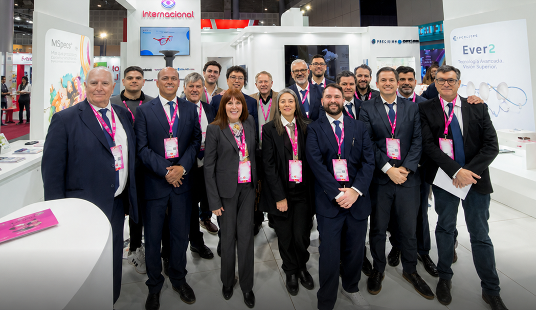 Group of professionals in suits at a trade show booth, wearing pink lanyards and name badges.
