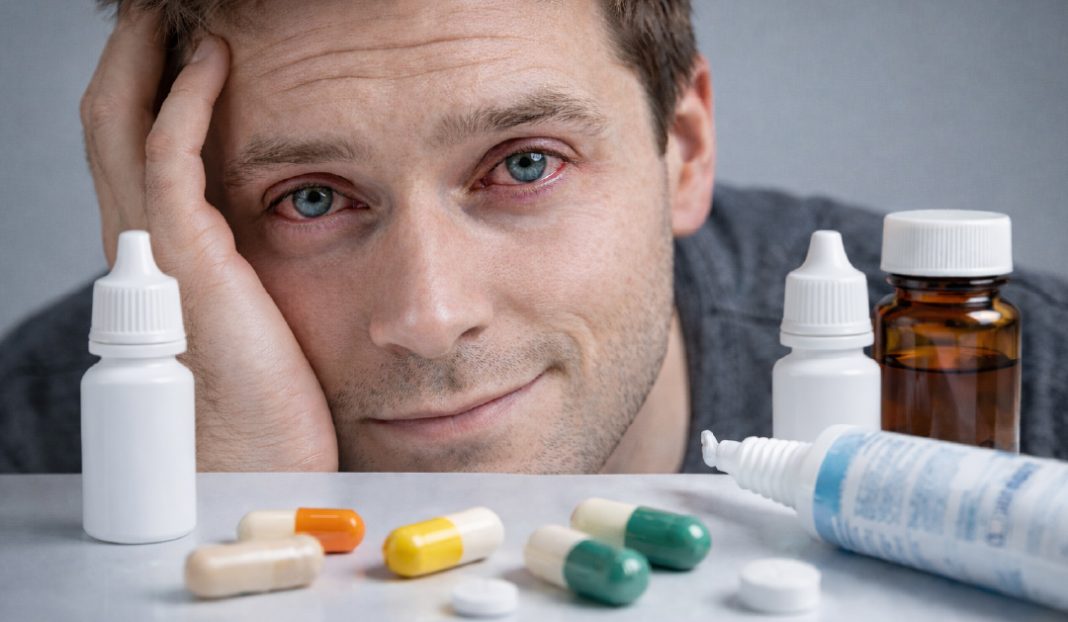 Tired man rests his head on his hand beside pills and medicine bottles on a table