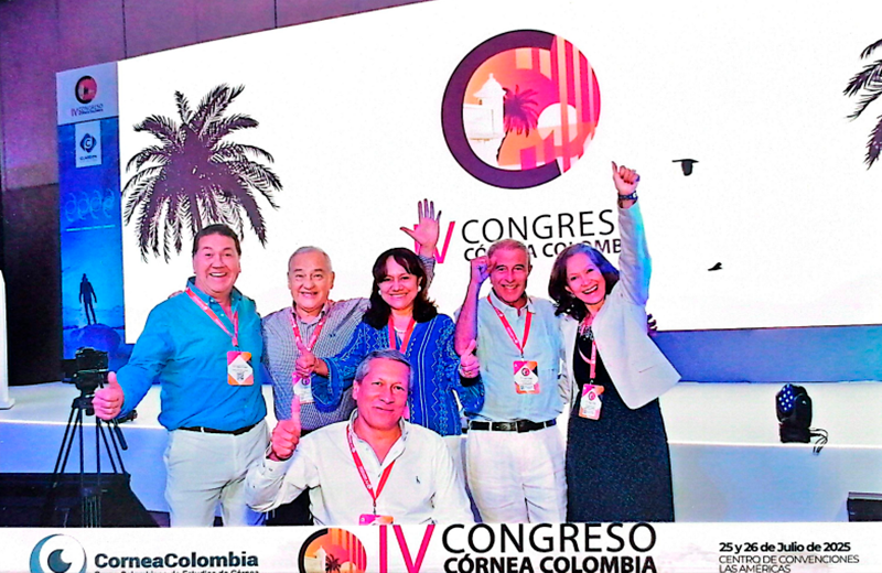 Six people on a conference stage posing with thumbs up; screen behind them shows the IV Congreso Cornea Colombia logo.