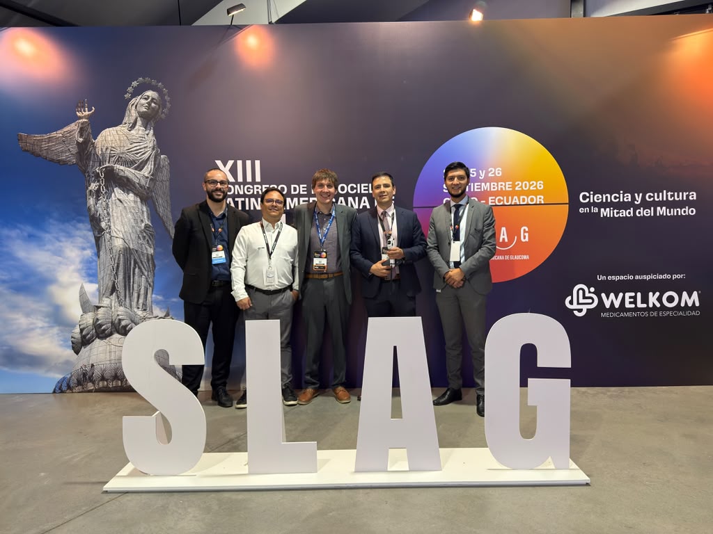 Five men in suits pose for a photo at a conference, standing behind large white letters spelling SLAG with a blue-purplish backdrop and event graphics in the background.